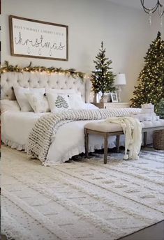 a bedroom decorated for christmas with white bedding and lights on the headboard, trees in