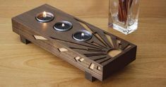 a candle holder made out of wood with three candles in it on a table next to a glass vase