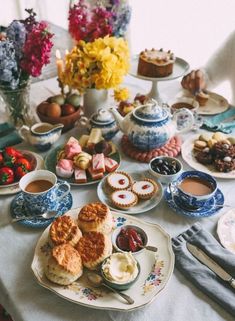 a table topped with plates and cups filled with desserts next to flowers on top of a white table cloth