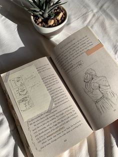 an open book sitting on top of a bed next to a small potted plant