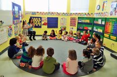 a group of children sitting on the floor in a circle talking to an adult teacher