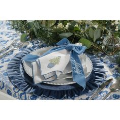 a blue and white table setting with napkins, silverware, and greenery