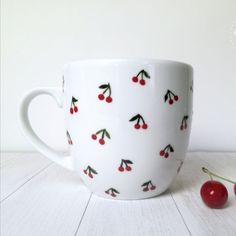 a white cup with cherries on it and two cherries next to the cup