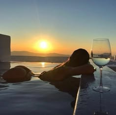 a woman sitting next to a glass of wine on top of a swimming pool at sunset