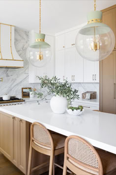 a white kitchen with marble counter tops and gold pendant lights hanging from the ceiling over the island