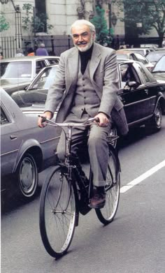 an old man riding a bike down the street in front of parked cars and other vehicles