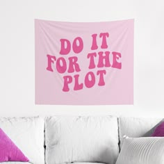 a pink wall hanging above a white couch with pillows on it and the words do it for the plot