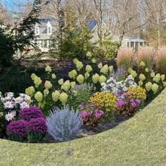 the garden is full of colorful flowers and plants in front of a large house with trees