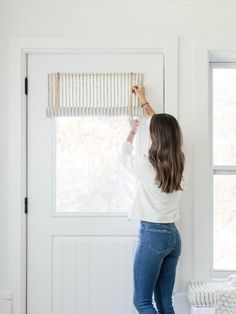 a woman is painting the wall with white paint and roller shades in her living room