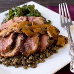 a white plate topped with meat and lentils next to a fork on a purple table cloth