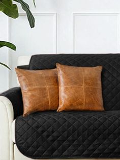 two brown pillows sitting on top of a black couch next to a potted plant