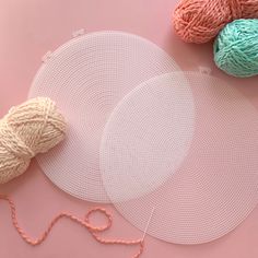 two balls of yarn next to each other on a pink surface with white netting around them