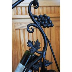 a wine bottle is hanging from a wrought iron rack with grapes and leaves on it