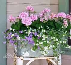 pink and white flowers in a metal planter on an old cart outside a house