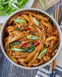 a bowl filled with noodles and vegetables on top of a wooden table next to chopsticks