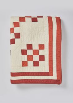 an orange and white quilted blanket with red squares on the bottom, sitting on a gray surface