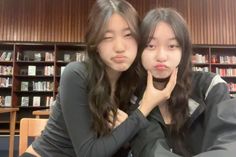 two young women sitting next to each other in front of bookshelves