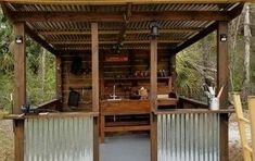 an outdoor bar in the woods with metal bars around it and stools next to it