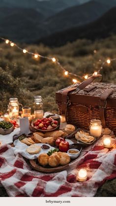 a picnic table with food and candles in the mountainside at night, lit up by string lights