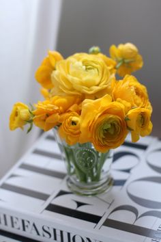 a vase filled with yellow flowers sitting on top of a table next to a book