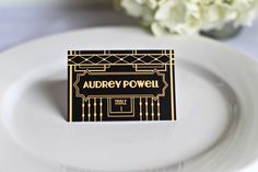 a white plate topped with a purple and gold place card on top of a table