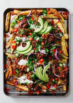 a tray filled with french fries covered in meat, avocado and other toppings