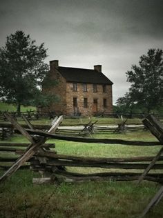 an old brick house sits in the middle of a field near a split rail fence