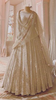 a white dress with gold sequins is on display in front of a window