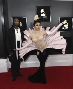 two people standing on a red carpet in front of an award winning dress and costume