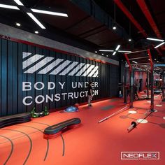 an indoor gym with red flooring and black walls that says body under construction on the wall