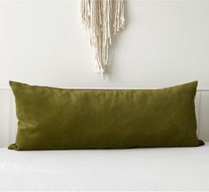 a green pillow sitting on top of a white bed next to a wall hanging with tassels