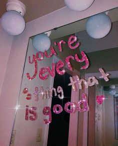 there is a mirror that has pink letters on it and balloons hanging from the ceiling