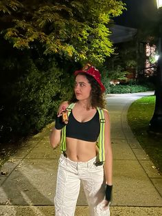 a woman in white pants and a black top is standing on the sidewalk at night