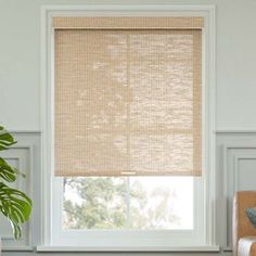 a living room with white walls and a window covered in beige roman blind shades that are hung on the windowsill