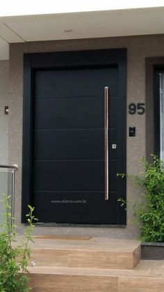 a black door on the side of a house with steps leading up to it and plants in front