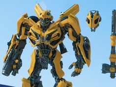 a yellow and black transformer robot next to a blue sky