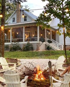 a fire pit in front of a white house with string lights strung around the porch