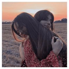 two women standing in an open field with the sun setting behind them and one holding her hair back