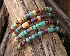 three bracelets with different colored beads sitting on top of a piece of driftwood