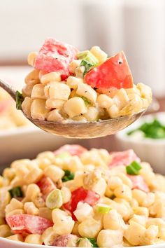 a spoon full of corn salad with tomatoes and spinach on it, ready to be eaten