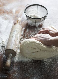 a person kneading dough on top of a wooden table next to a rolling pin