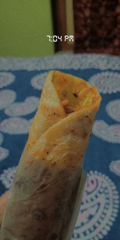 a hand holding a burrito on top of a blue tablecloth covered table cloth