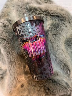 a purple and black tumbler with the word mom on it sitting on a fur rug