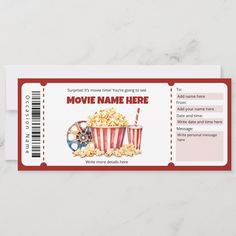 a red and white movie ticket sitting on top of a marble counter next to a cup of popcorn