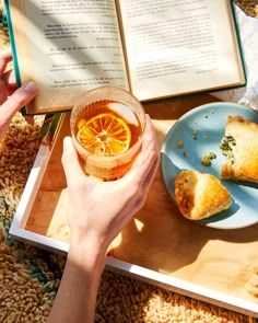 a person holding an open book over a plate with food on it and a drink in front of them