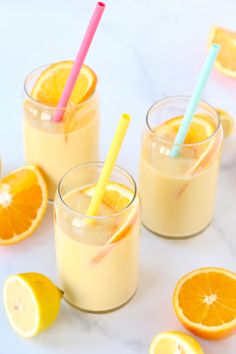 three glasses filled with orange juice and straws next to sliced lemons on a table