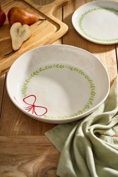 two white bowls with green designs on them sitting on a wooden table next to pears