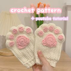 a person holding up two crocheted animal paw mitts on top of a wooden table