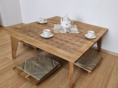 a wooden table with tea cups and saucers on it, next to two stools