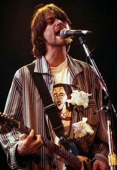 a man holding a guitar while standing in front of a microphone and wearing a striped shirt